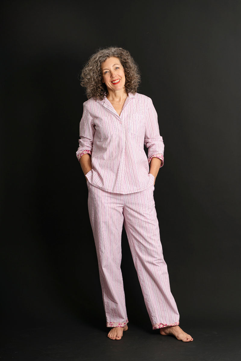 Woman wearing the Havana Pajamas sewing pattern from Liesl + Co on The Fold Line. A pyjamas pattern made in cotton poplin, twill, sateen, flannel, lawn, voile, linen, or rayon fabric, featuring a popover-style top with a convertible camp collar, front pockets, a back yoke with an inverted box pleat, long sleeves, and side vents, and trousers with an elastic waist, pockets, and cuffed hems.