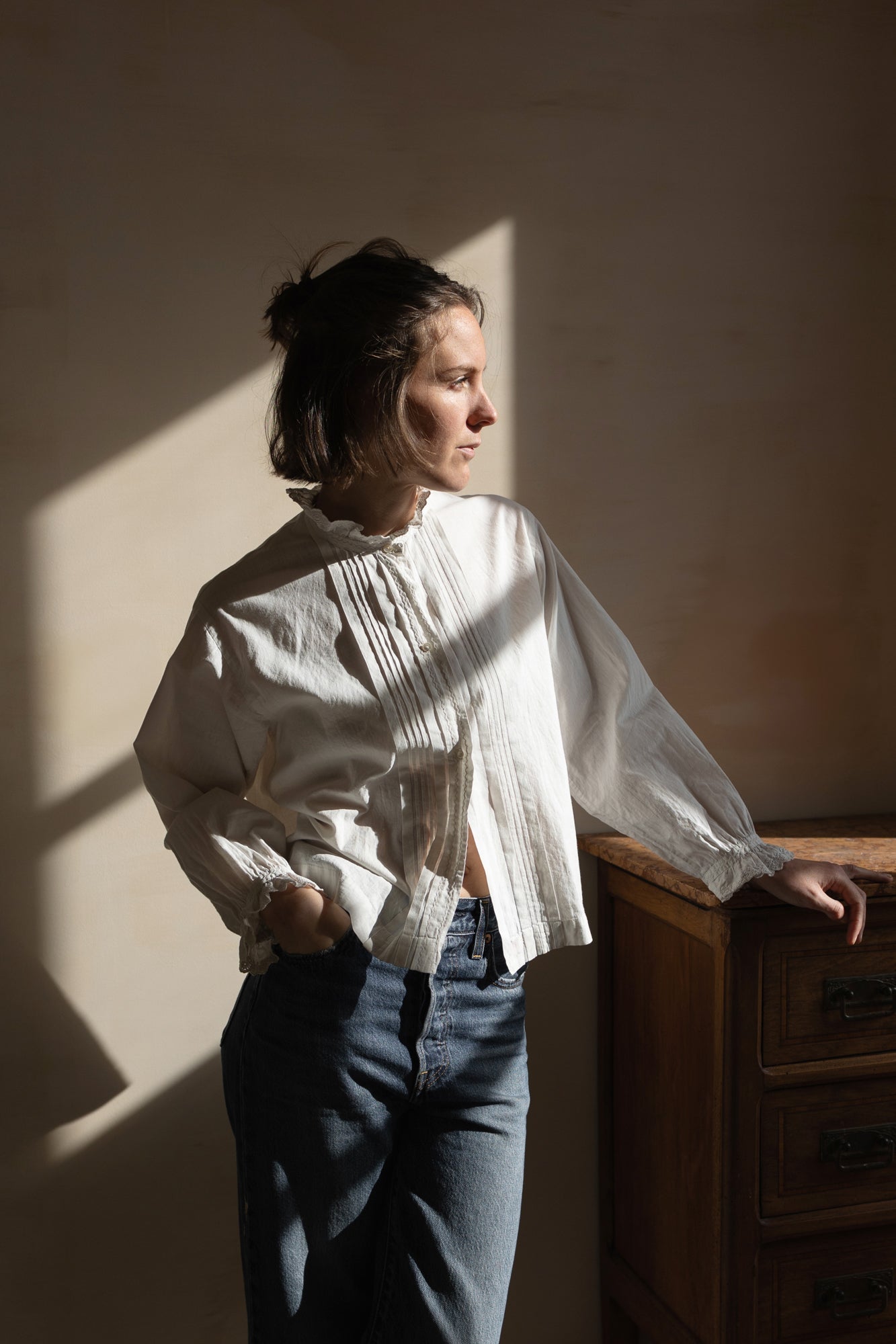 Woman wearing the Henriette Blouse sewing pattern from Ready to Sew on The Fold Line. A shirt pattern made in cotton poplin, linen, linen/cotton blend, silk, or tencel fabric, featuring a round neckline with a lace ruffle, pintucks, button front, long sleeves, and a short boxy fit.