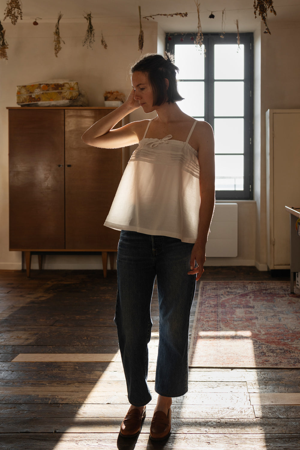Woman wearing the Holly Top sewing pattern from Ready to Sew on The Fold Line. A vintage-inspired camisole pattern made in cotton, linen, tencel, or silk fabric, featuring an airy silhouette, thin straps, pintucks, and a drawstring tie.