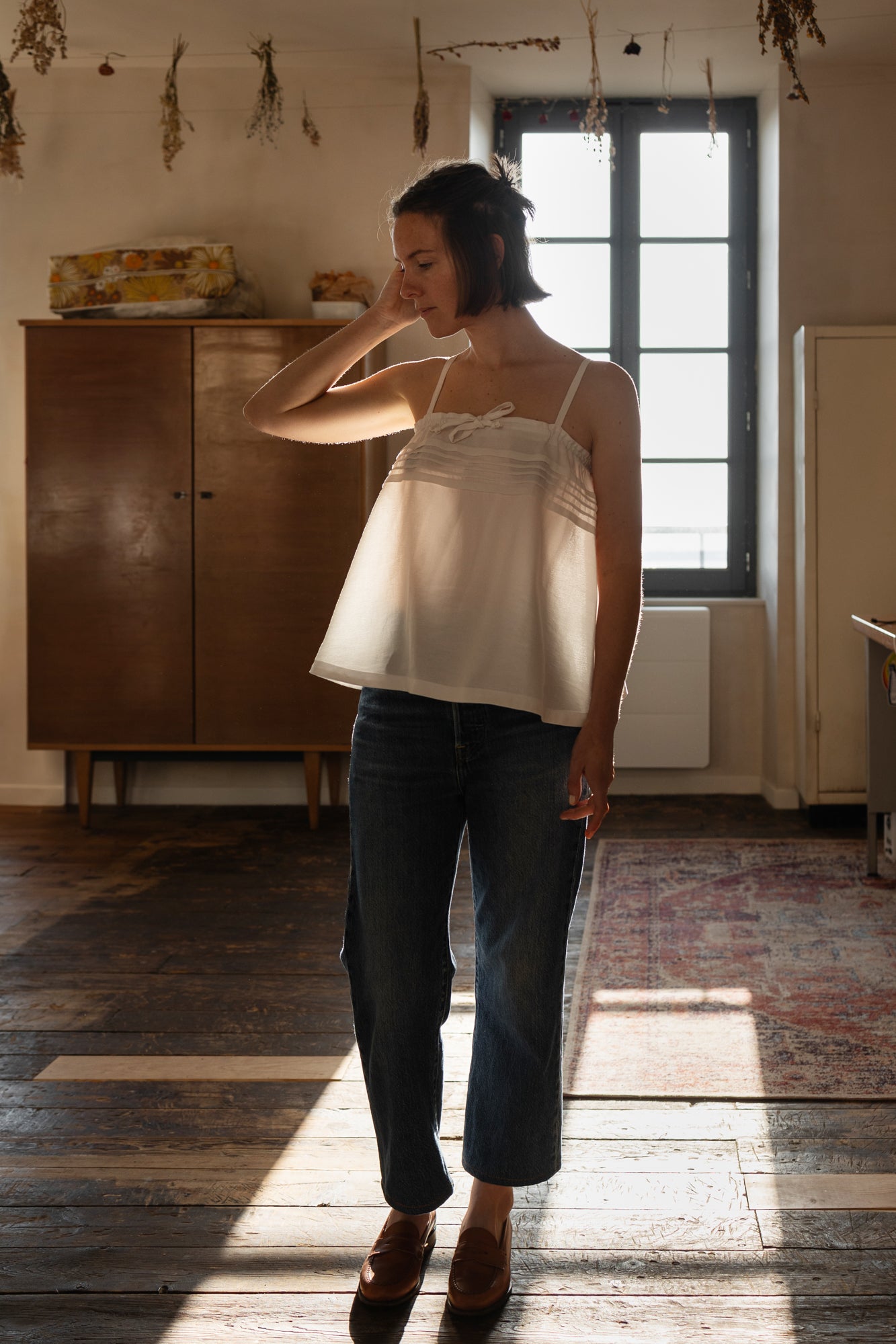 Woman wearing the Holly Top sewing pattern from Ready to Sew on The Fold Line. A vintage-inspired camisole pattern made in cotton, linen, tencel, or silk fabric, featuring an airy silhouette, thin straps, pintucks, and a drawstring tie.