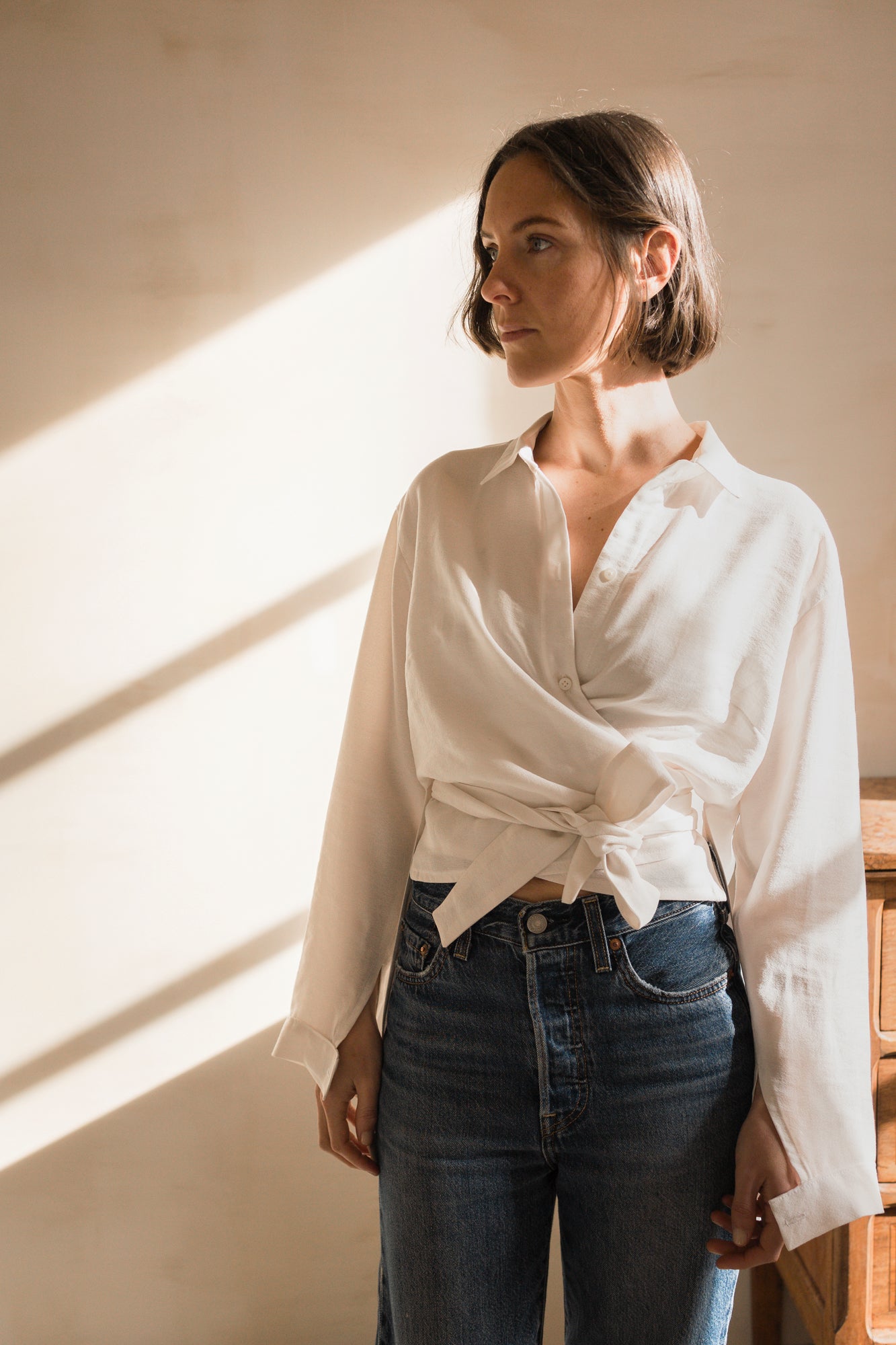 Woman wearing the Hortense Shirt sewing pattern from Ready to Sew on The Fold Line. A shirt pattern made in lightweight linen, tencel, or cotton fabric, featuring a relaxed fit, wrap front with a shirt collar, and long sleeves.