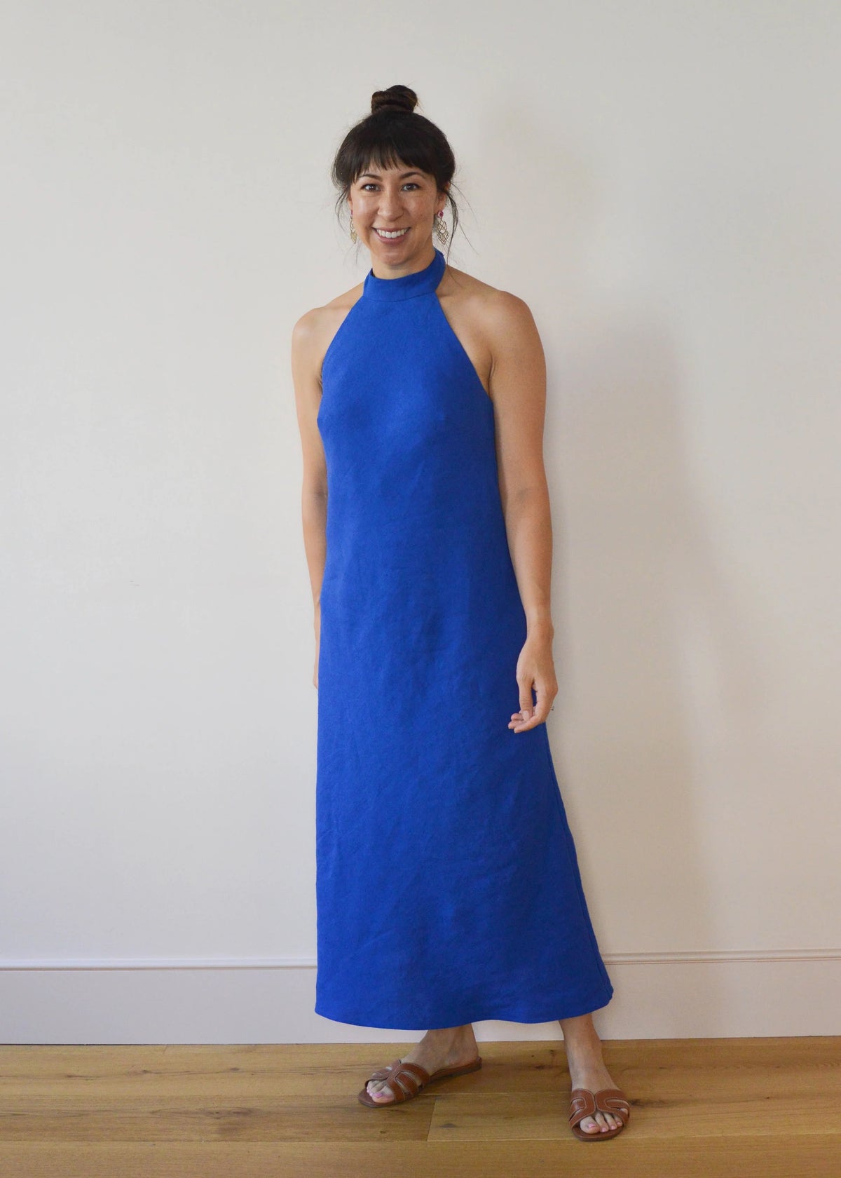 Woman wearing the Hoxton Halter-Neck Dress sewing pattern from Nina Lee on The Fold Line. A sleeveless dress pattern made in crepe, viscose, silk, or linen fabric, featuring a bias cut, bust darts, scooped back, high neck with tie, and above ankle length.