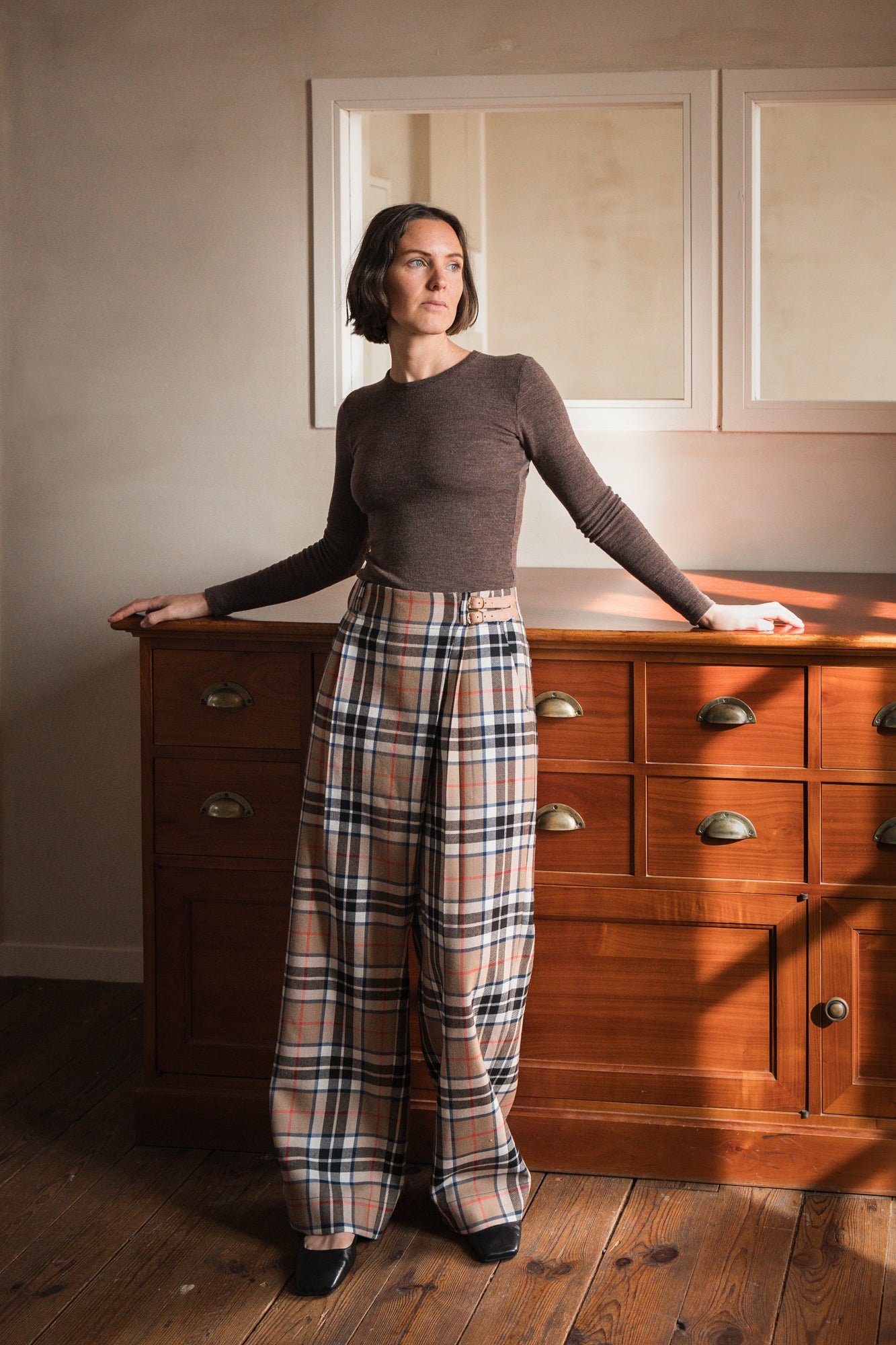 Woman wearing the Hugo Wrap Pants sewing pattern from Ready to Sew on The Fold Line. A trousers pattern made in tencel twill, tencel or wool crepe, linen/tencel or linen/cupro blend fabric, featuring a fitted waistband, asymmetrical closure, soft pleats, pockets, and straight legs.
