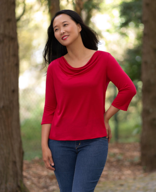 Woman wearing the Iguazu Top sewing pattern from Itch to Stitch on The Fold Line. A top pattern made in knit fabric with a fluid drape, featuring a draped cowl neckline and 3/4 length sleeves.