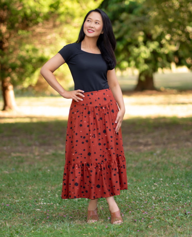 Woman wearing the Irazu Skirt sewing pattern from Itch to Stitch on The Fold Line. A skirt pattern made in crepe, tencel twill, linen/rayon blends, or rayon, viscose, or modal challis fabric, featuring front and back yokes with gathers, an invisible side zipper, elastic sewn into the back waist, in-seam pockets, a hem ruffle, and midi length.