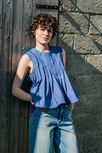Woman wearing the Isola Top sewing pattern from Fibre Mood on The Fold Line. A sleeveless top pattern made in poplin, linen, silk, or broderie anglaise fabric, featuring a round neckline and pleats stitched into place for a peplum effect.