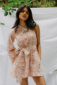 Woman wearing the Ivy Dress sewing pattern from NH Patterns on The Fold Line. A dress pattern made in lightweight cotton, cotton chambray, linen, tencel, or rayon/viscose fabric, featuring a one-shoulder design, bell sleeve, elastic waist, tie belt, and mini length.