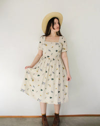 Woman wearing the Ivy Dress sewing pattern from Oh Me Oh My Sewing on The Fold Line. A dress pattern made in quilting cotton or plain weave cotton fabric, featuring a square neckline, princess seams, V-shaped waist, short puff sleeves, and midi length.