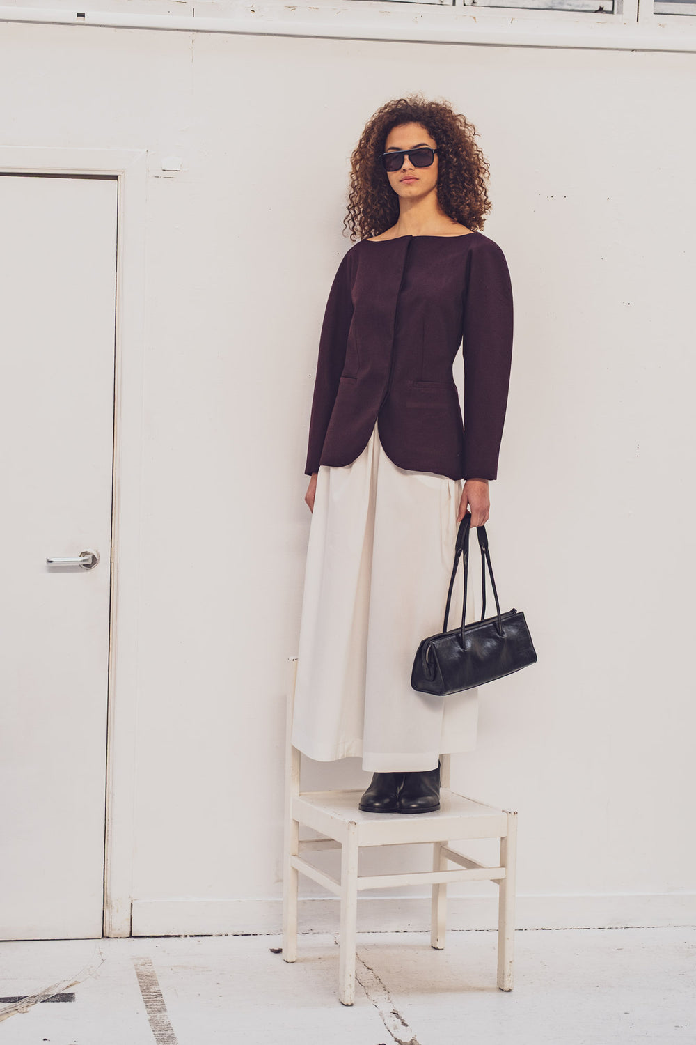 Woman wearing the Jacoba Blazer sewing pattern from Fibre Mood on The Fold Line. A lined jacket pattern made in light denim, cotton twill, gabardine, cotton satin, or light canvas fabric, featuring a wide neckline, concealed button closure, grown-on balloon sleeves, and welt pockets. 