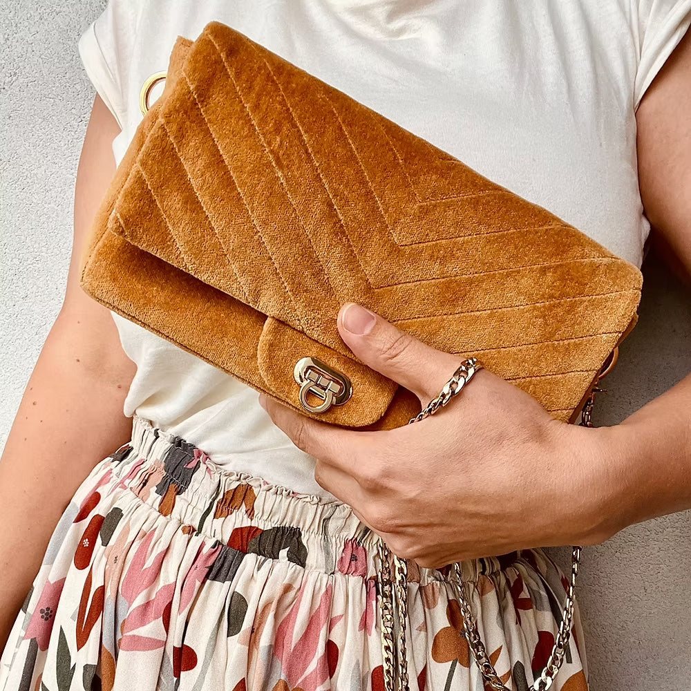 Woman holding the Juno Handbag sewing pattern from Sew.lala Patterns on The Fold Line. A bag pattern made in canvas, leather, or jacquard fabric, featuring a rectangular shape, internal pocket, metal clasp, and bag chain strap.