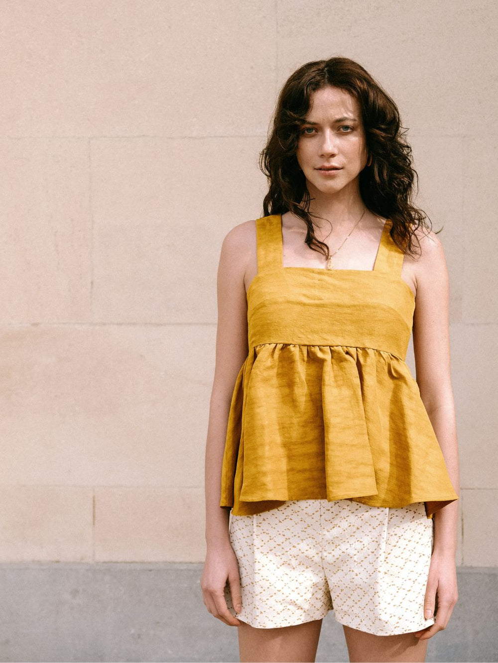 Woman wearing the Kaiko Top sewing pattern from Notches on The Fold Line. A sleeveless top pattern made in cotton, viscose, chiffon, embroidery, jacquard, or denim fabric, featuring wide straps, a square neckline, and gathered peplum.