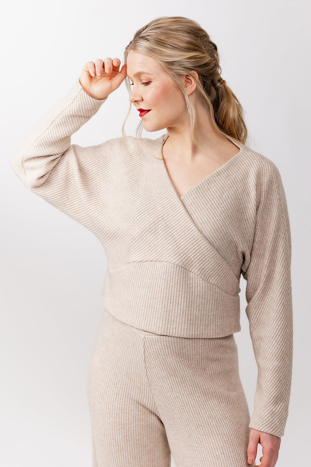 Woman wearing the Kajo Wrap Sweater sewing pattern from Named on The Fold Line. A top pattern made in medium weight knit fabric, featuring a relaxed fit, V-neck, long batwing sleeves, and curved hem band.