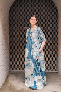 Woman wearing the Kaori Dress sewing pattern from Fibre Mood on The Fold Line. A dress pattern made in poplin, cotton sateen, linen, nylon, taffeta, crepe, viscose satin, chambray, seersucker, lyocell, or double gauze fabric, featuring a loose fit, elbow length raglan sleeves, a deep neckline with eyelets and lacing, side seam pockets, and maxi length.