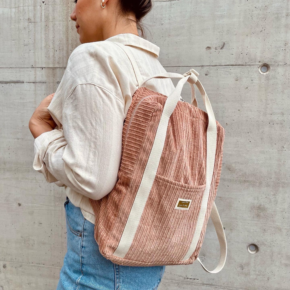 Woman wearing the Kayli Backpack sewing pattern from Sew.lala Patterns on The Fold Line. A backpack pattern made in canvas or oilskin fabric, featuring size-adjustable shoulder straps, top handles, a zipper closure, and outside and inside pockets.