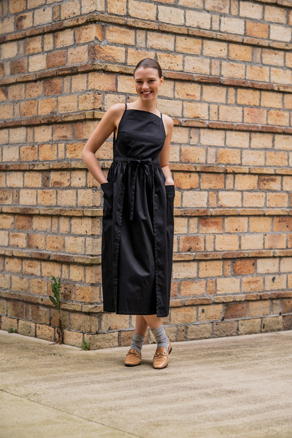 Woman wearing the Khloe Dress sewing pattern from Fibre Mood on The Fold Line. A wrap dress pattern made in poplin, lyocell, linen, double gauze, broderie anglaise, chambray, woven jacquard, or (viscose) crepe fabric, featuring spaghetti straps, an apron neckline, gathered skirt, and large patch pockets.