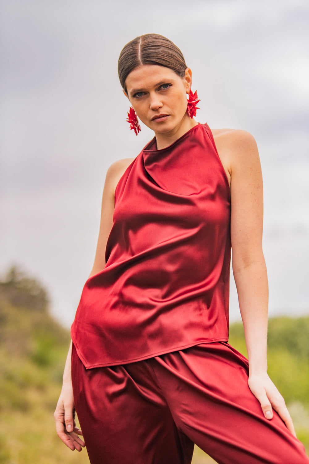 Woman wearing the Kiri Top sewing pattern from Fibre Mood on The Fold Line. A sleeveless top pattern made in satin, acetate, charmeuse, silk, viscose (crepe), lyocell, or chambray fabric, featuring a halter neck, draped front, and asymmetrical hem.