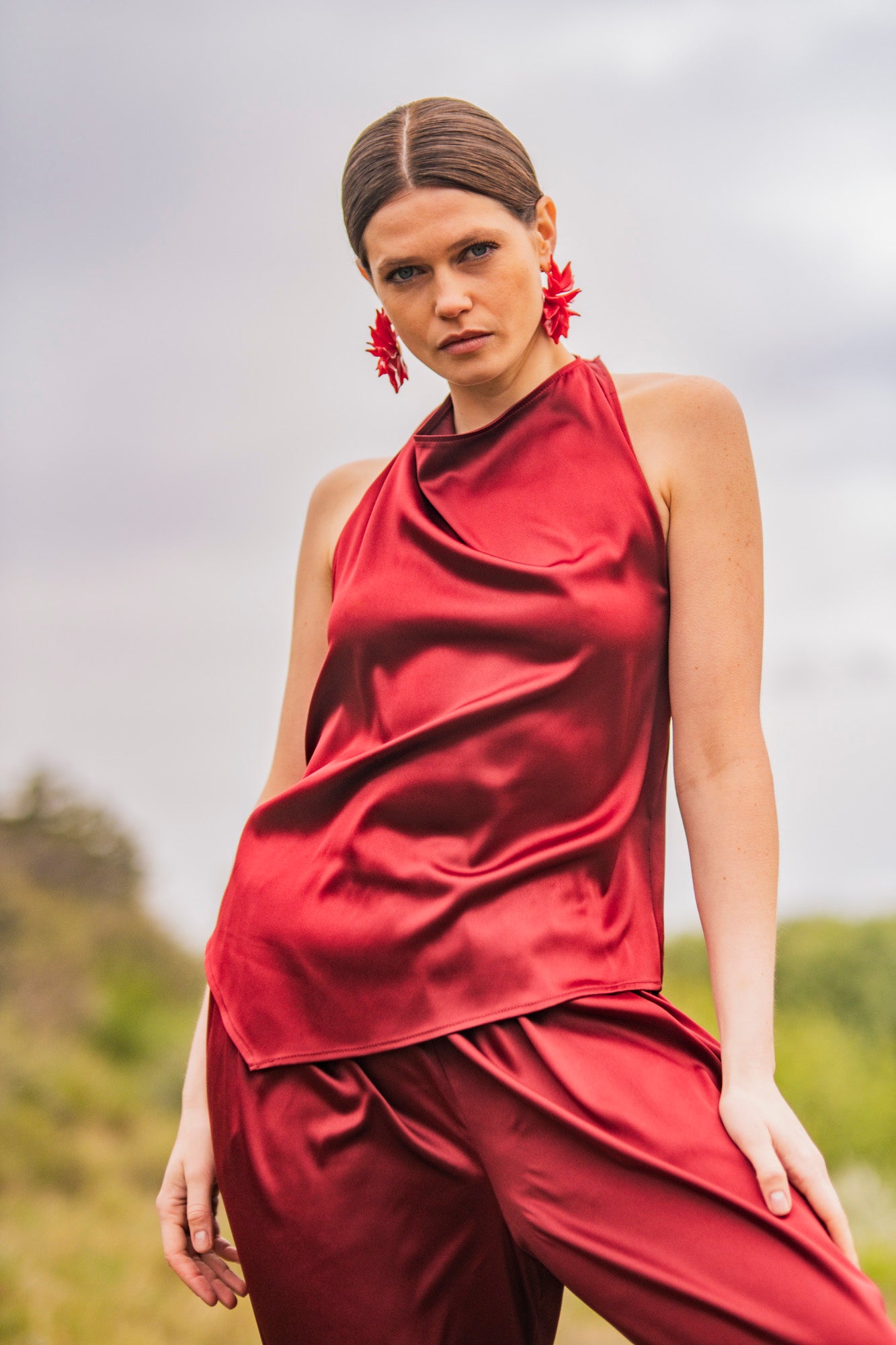 Woman wearing the Kiri Top sewing pattern from Fibre Mood on The Fold Line. A sleeveless top pattern made in satin, acetate, charmeuse, silk, viscose (crepe), lyocell, or chambray fabric, featuring a halter neck, draped front, and asymmetrical hem.