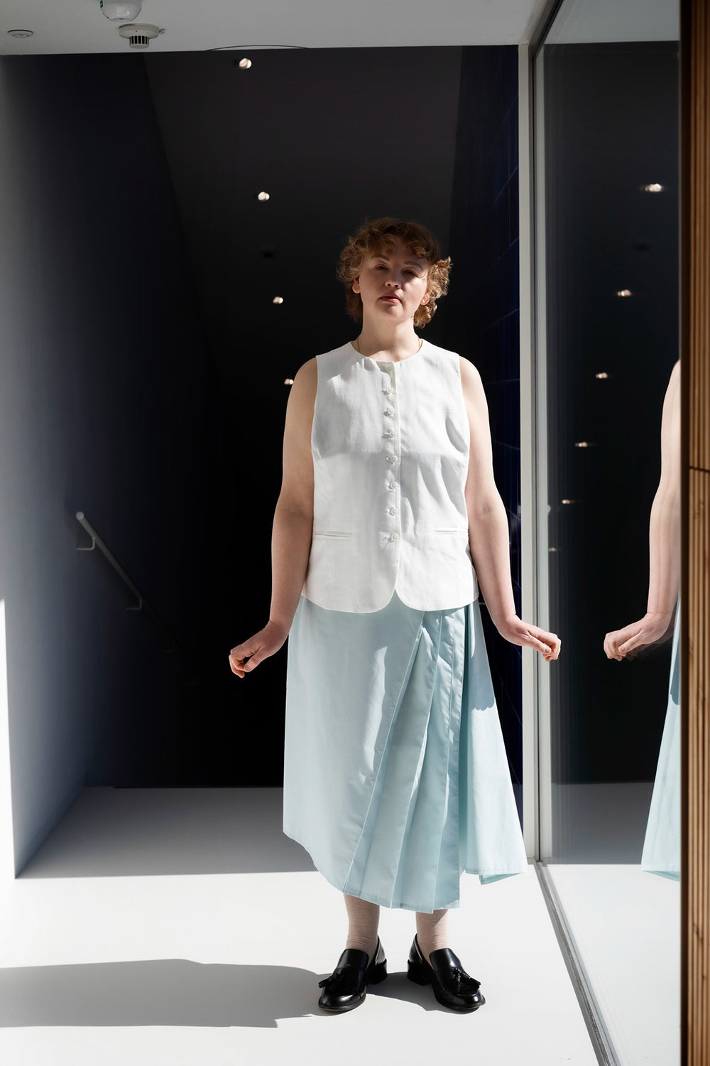 Woman wearing the Kirsti Skirt sewing pattern from TAUKO on The Fold Line. A skirt pattern made in medium weight woven fabric, featuring an asymmetrical silhouette with a side godet and pleats, side zip, and midi length.