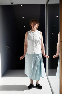 Woman wearing the Kirsti Skirt sewing pattern from TAUKO on The Fold Line. A skirt pattern made in medium weight woven fabric, featuring an asymmetrical silhouette with a side godet and pleats, side zip, and midi length.