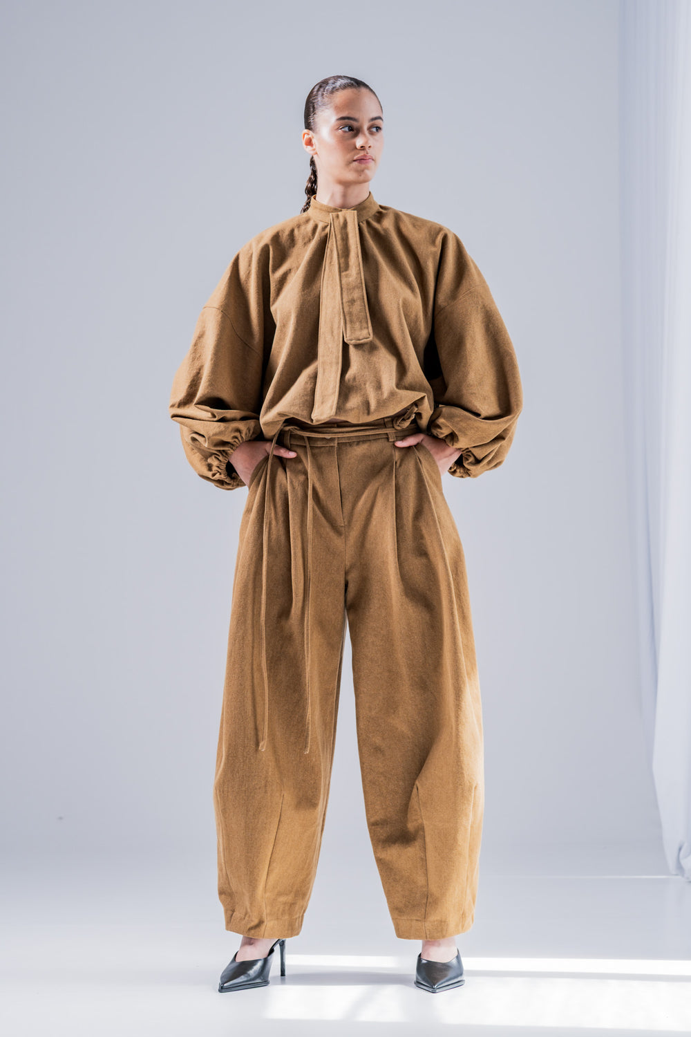 Woman wearing the Kiva Trousers sewing pattern from Fibre Mood on The Fold Line. A trousers pattern made in gabardine, cotton twill, poplin, corduroy, denim, linen, viscose crepe, or modal fabric, featuring pleats at the waist, darts at the hem, slanted side pockets, a fly front, and belt loops. 