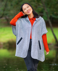 Woman wearing the Koersel Cape sewing pattern from Itch to Stitch on The Fold Line. A cape pattern made in coating, wool blend, or double knit fabric, featuring an open front, elbow-length sleeves, an oversized hood, welt pockets, and mid-thigh length.