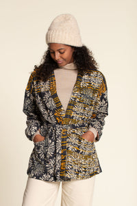 Woman wearing the Komi Jacket sewing pattern from Wardrobe by Me on The Fold Line. An unlined jacket pattern made in cotton, linen, double gauze, quilted, or jersey fabric, featuring a wrap front with a belt, dropped shoulders, and deep pockets.