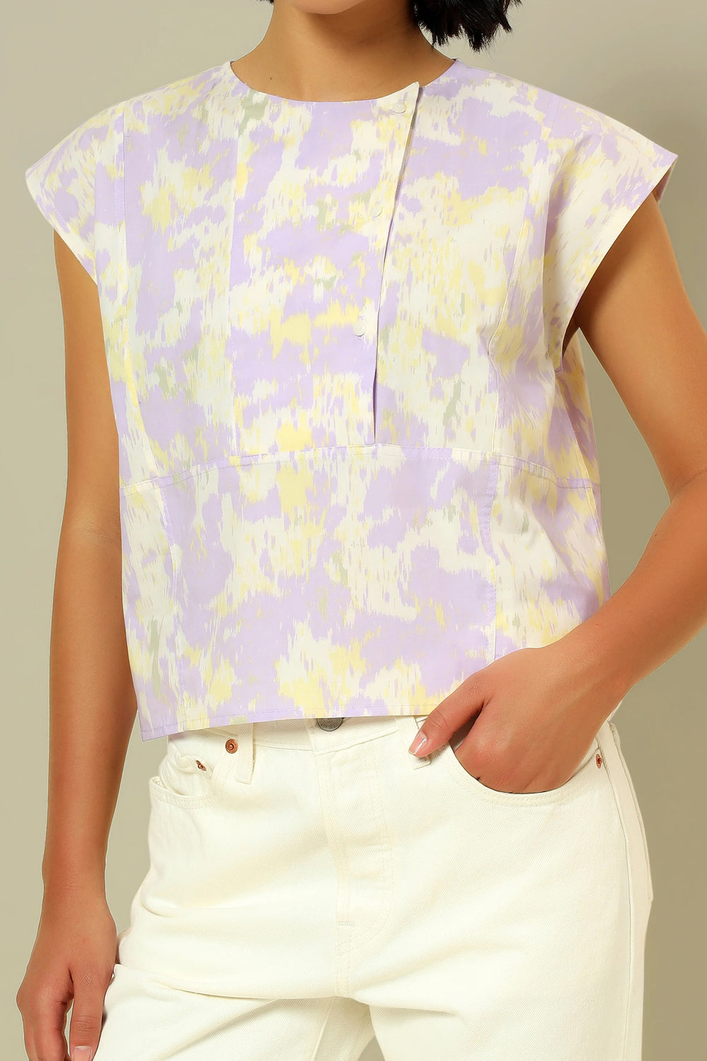 Woman wearing the La Blouse Sculpturale sewing pattern from Atelier Brunette on The Fold Line. A sleeveless top pattern made in cotton, linen, or soft denim fabric, featuring a round neckline, buttoned bib, and flat felled seams.