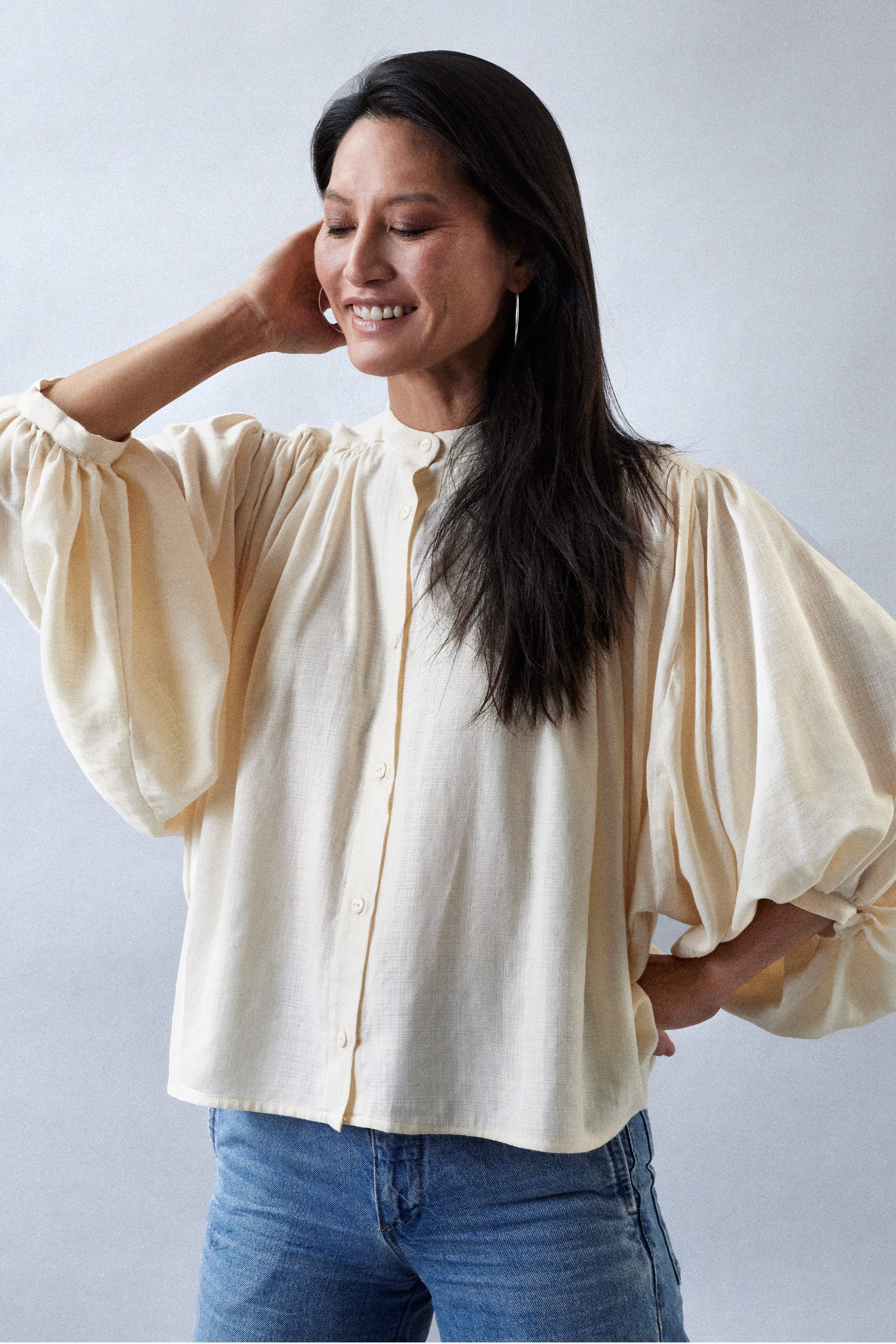 Woman wearing the La Blouse sewing pattern from Atelier Brunette on The Fold Line. A shirt pattern made in viscose, linen, or cotton fabric, featuring an oversized cut, voluminous gathers, officer collar, front button placket, lined back yoke, and batwing sleeves gathered into cuffs.