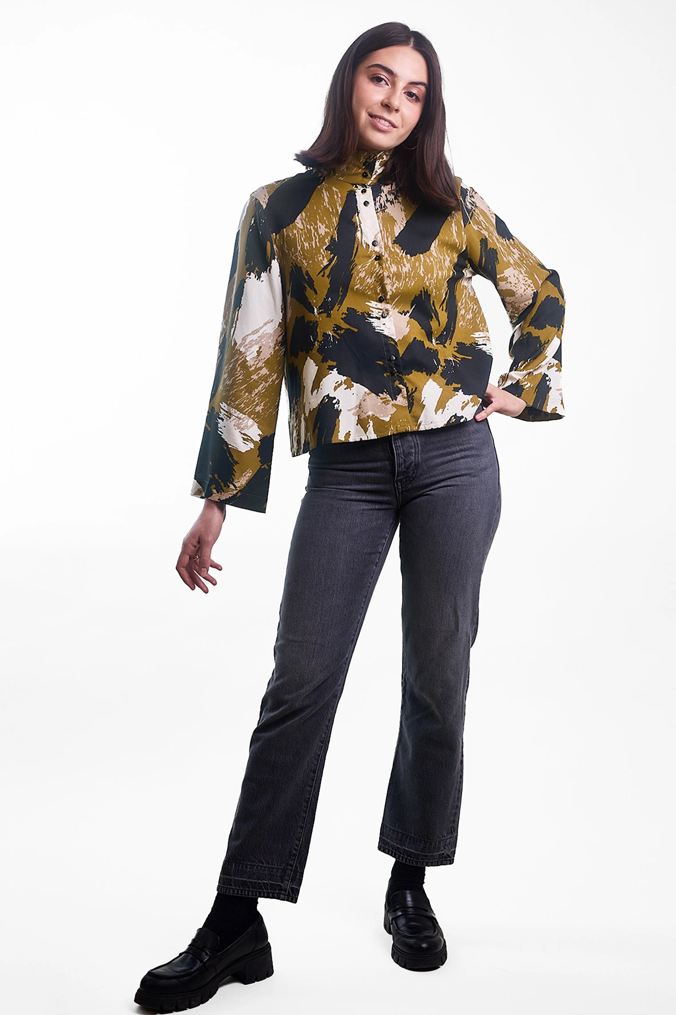 Woman wearing the La Chemise Amirale sewing pattern from Atelier Brunette on The Fold Line. A shirt pattern made in viscose, viscose blend, linen, or linen blend fabric, featuring a loose fit, high collar, double-button front placket, back yoke and pleats, and long, slightly flared sleeves.