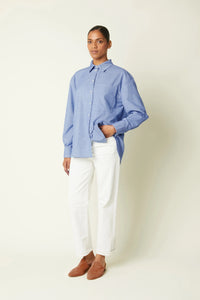 Woman wearing the La Chemise Boyish sewing pattern from Atelier Brunette on The Fold Line. A shirt pattern made in cotton or cotton blend, poplin, linen, viscose, lightweight gabardine, or lightweight corduroy fabric, featuring a loose fit, straight cut, collar and stand, unique back yoke detail, long sleeves with buttoned cuffs, patch pocket, and shirttail hem.