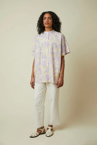 Woman wearing the La Chemisette Structurée sewing pattern from Atelier Brunette on The Fold Line. A top pattern made in cotton Oxford, poplin, striped cotton, printed Ikat, or woven velvet fabric, featuring a relaxed fit, curved yokes, grown-on short sleeves, a stand collar, and button placket.