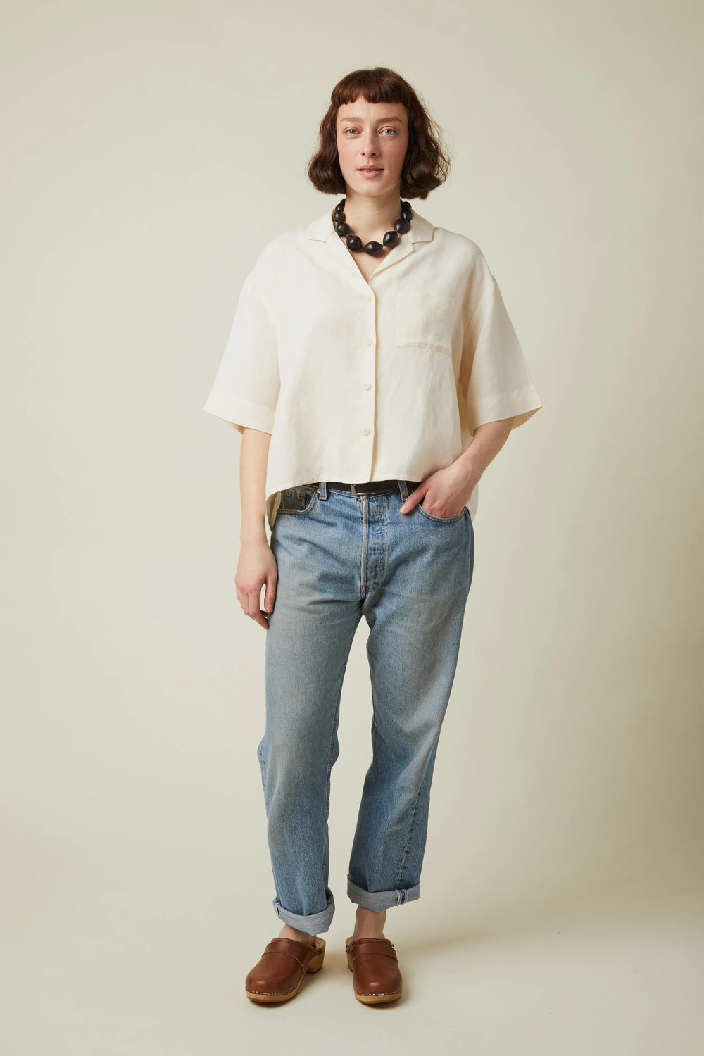 Woman wearing the La Chemisette sewing pattern from Atelier Brunette on The Fold Line. A shirt pattern made in viscose, cotton, cotton double gauze, cotton-linen blend, or linen-viscose blend fabric, featuring a boxy shape, collar, front button placket, back yoke with pleat, chest pocket, and elbow length sleeves.