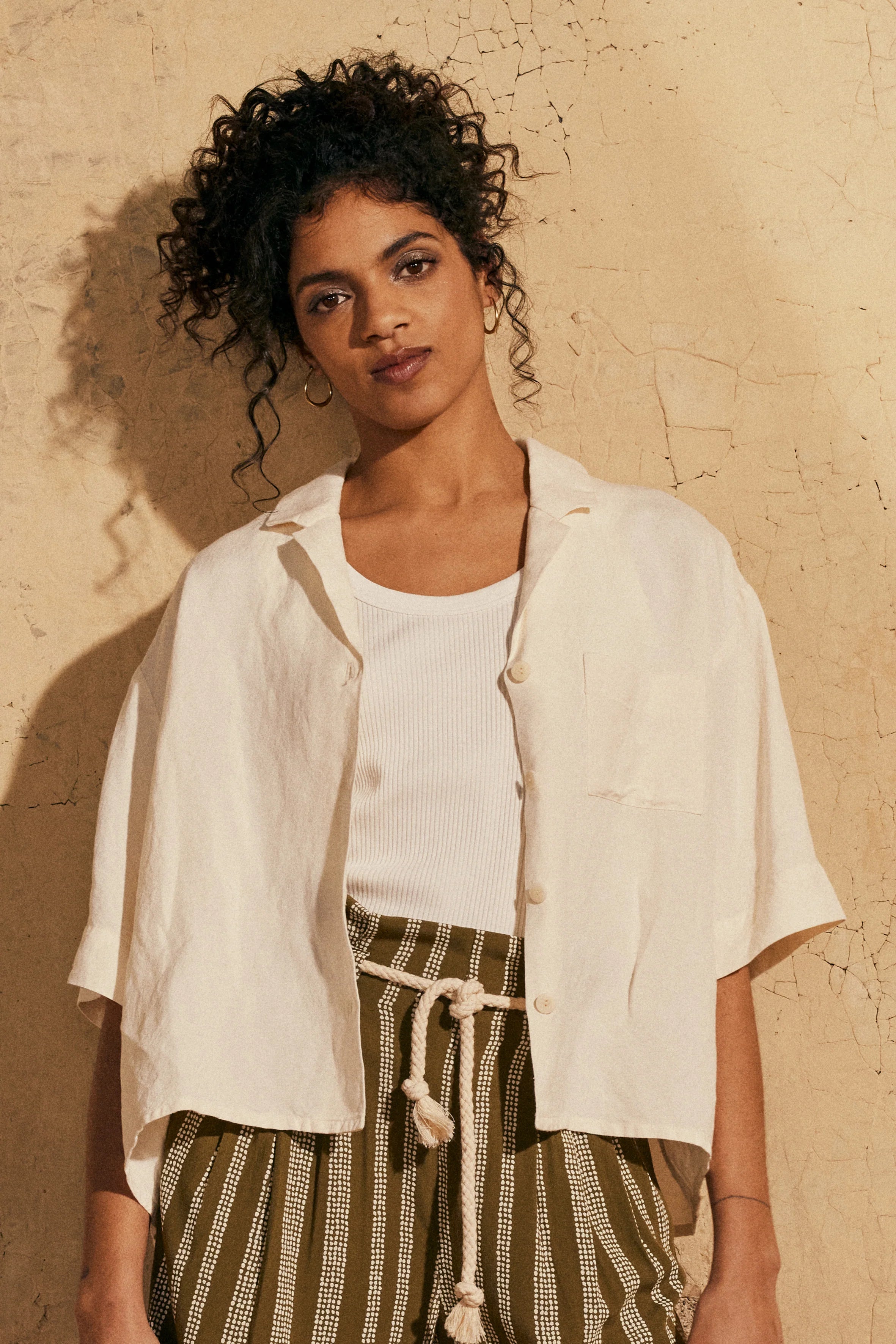 Woman wearing the La Chemisette sewing pattern from Atelier Brunette on The Fold Line. A shirt pattern made in viscose, cotton, cotton double gauze, cotton-linen blend, or linen-viscose blend fabric, featuring a boxy shape, collar, front button placket, back yoke with pleat, chest pocket, and elbow length sleeves.