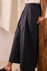 Woman wearing the La Jupe Culotte sewing pattern from Atelier Brunette on The Fold Line. A culottes pattern made in cotton or cotton blend, poplin, linen, viscose or viscose blend fabric, featuring a relaxed fit, high waist, elasticated back waistband, front pleats, button placket on one side, pocket on the other, and 7/8 length.