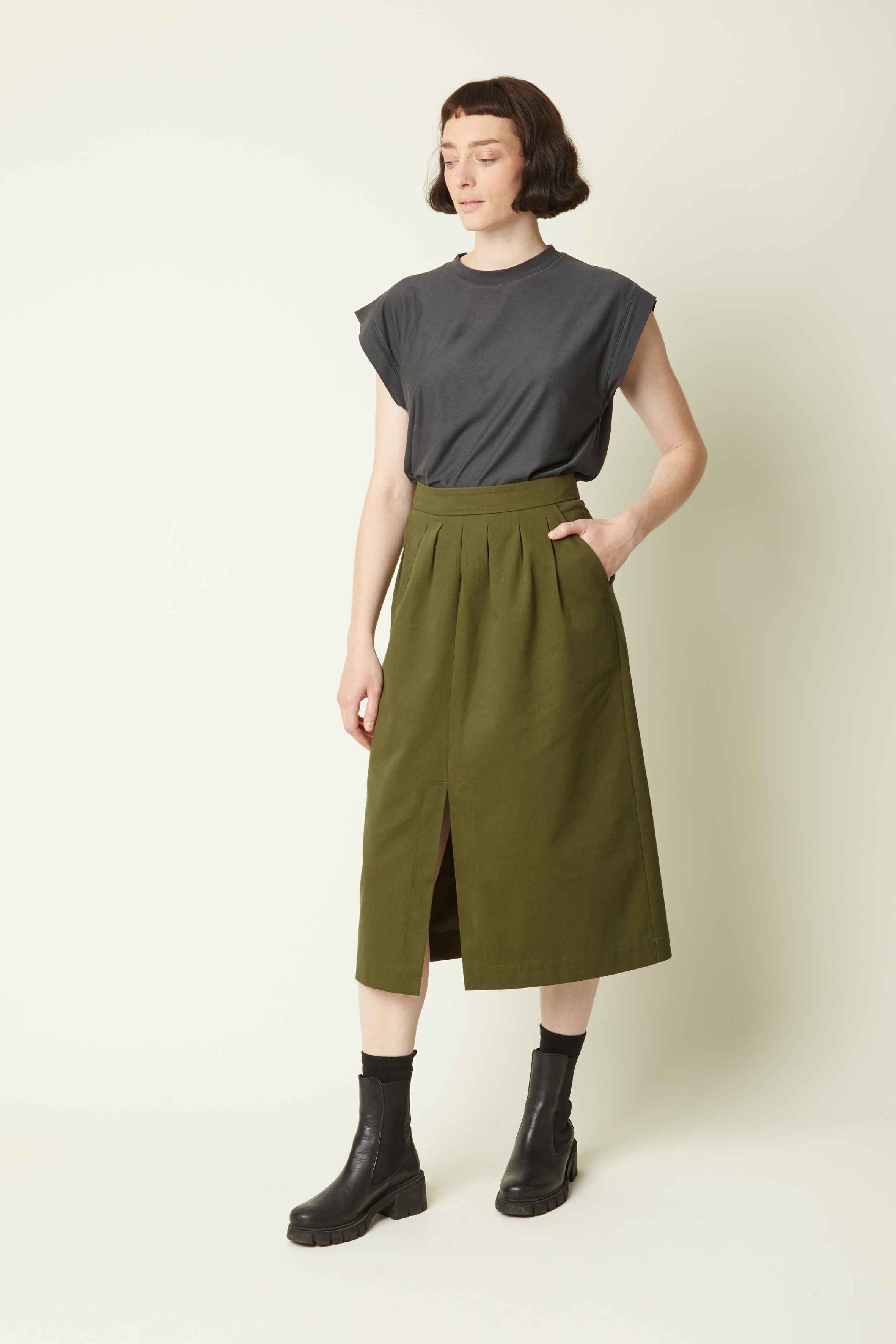 Woman wearing the La Jupe Défendue sewing pattern from Atelier Brunette on The Fold Line. A skirt pattern made in corduroy, gabardine, viscose, or viscose blend fabric, featuring a pleated front, front slit, side pockets, and midi length.