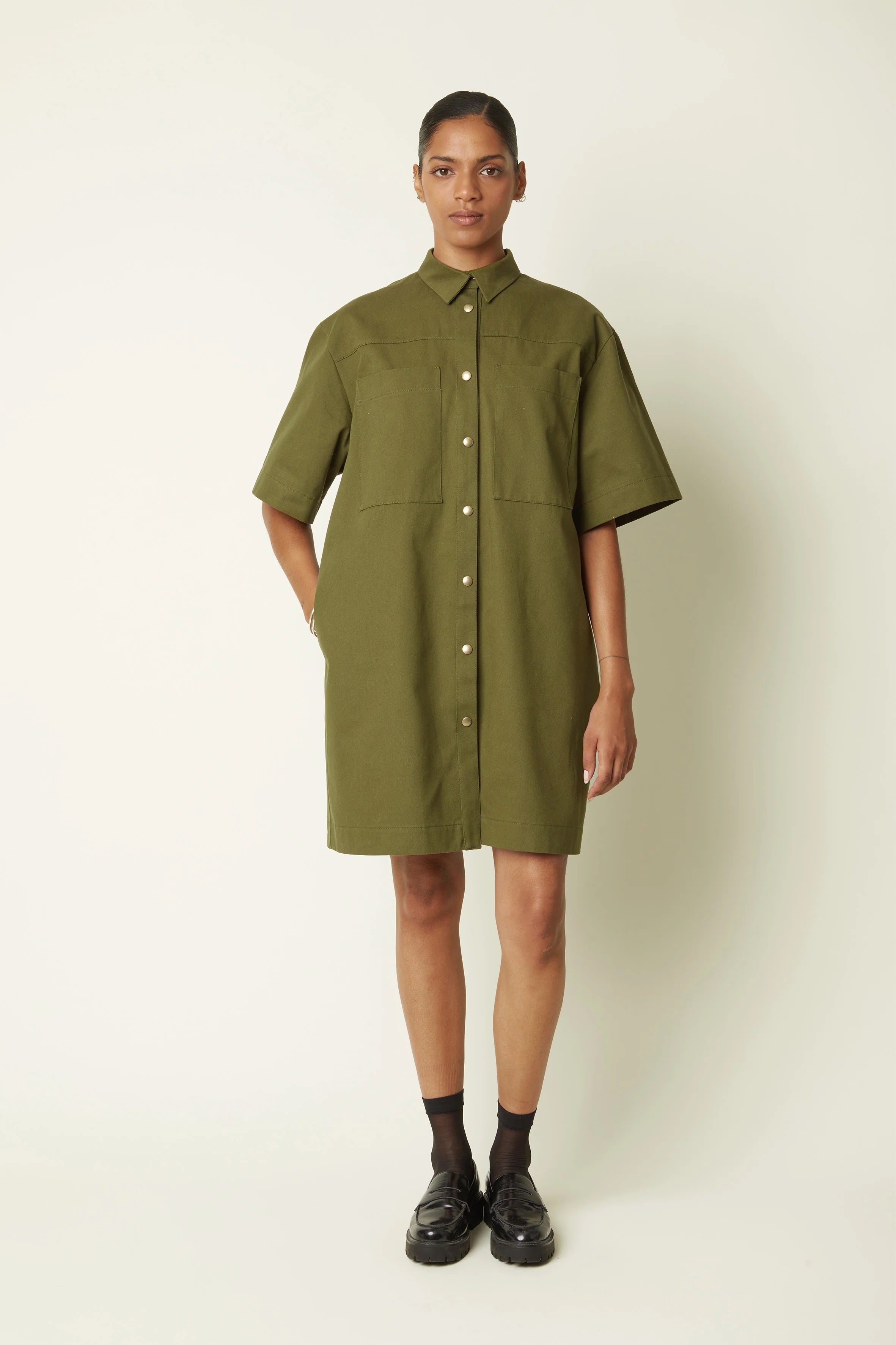 Woman wearing the La Petite Robe sewing pattern from Atelier Brunette on The Fold Line. A shirt dress pattern made in denim, cotton gabardine, cotton blend, or corduroy fabric, featuring a slightly oversized fit, shirt collar, front and back yokes, front button placket, elbow length sleeves, side and patch pockets, and above knee length.