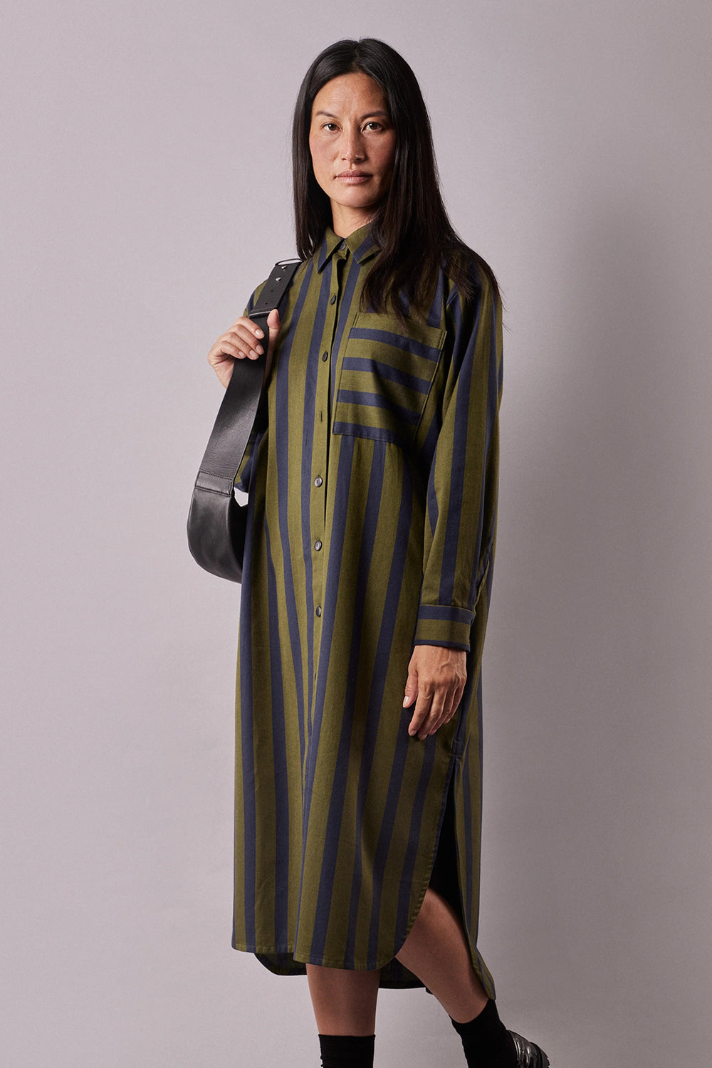 Woman wearing the La Robe Chemise sewing pattern from Atelier Brunette on The Fold Line. A shirt dress pattern made in cotton, viscose, or linen fabric, featuring a relaxed fit, shirt collar, front button placket, chest pocket, back yoke with gathers, long sleeves with cuffs, side slits, and midi length.