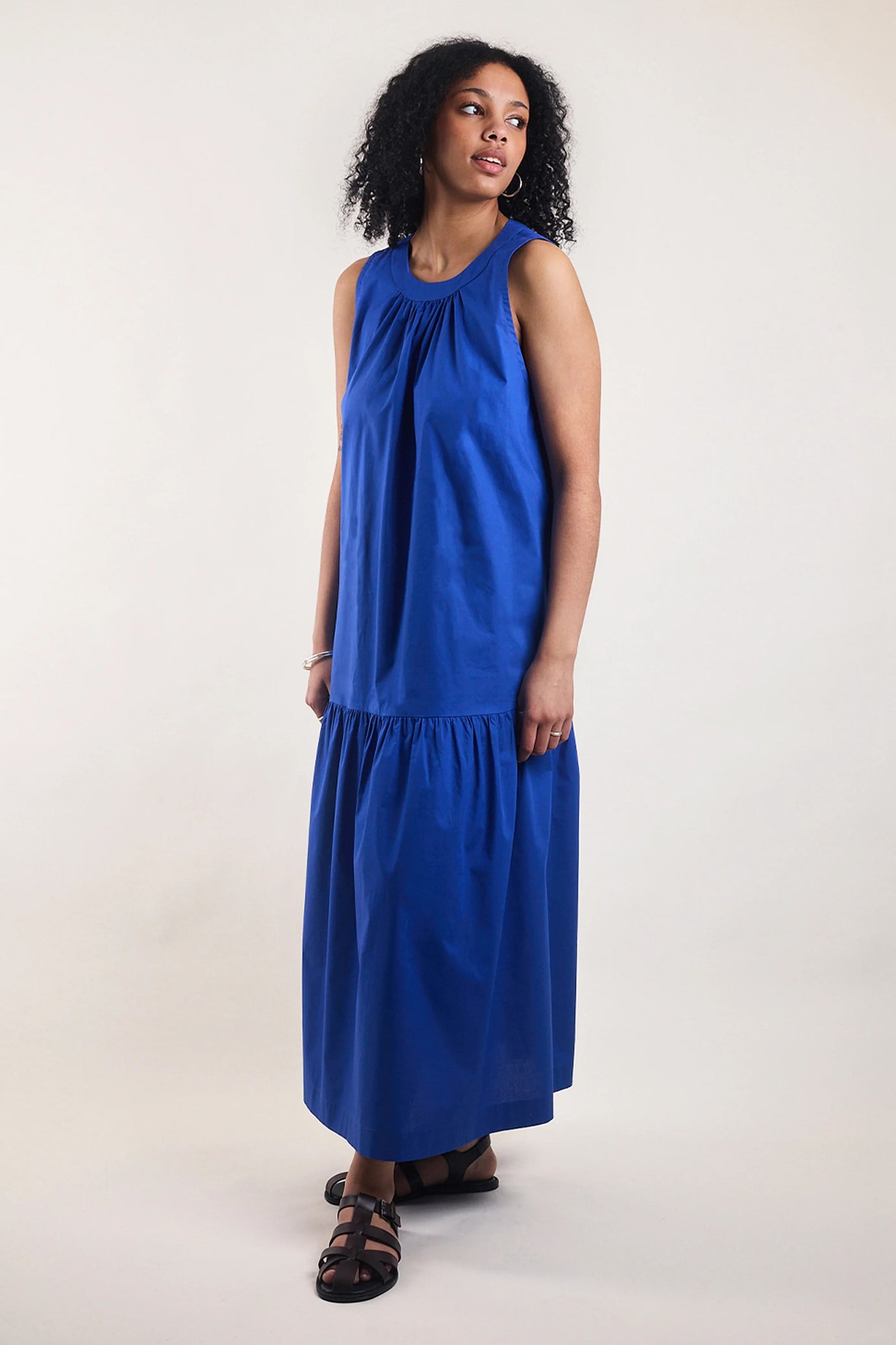 Woman wearing the La Robe Flare sewing pattern from Atelier Brunette on The Fold Line. A sleeveless dress pattern made in cotton or cotton blend, poplin, linen, viscose or viscose blend fabric, featuring a relaxed fit, round neckline, dropped gathered skirt tier, and maxi length.