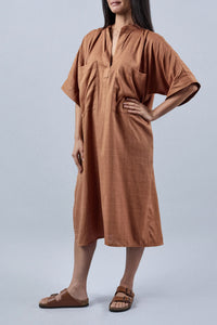 Woman wearing the La Robe Tunique sewing pattern from Atelier Brunette on The Fold Line. A dress pattern made in linen, cotton, linen-cotton blend, linen-rayon blend, rayon, double gauze, or lightweight gabardine fabric, featuring a relaxed fit, stand collar, open front placket, gathers at the shoulders and back yoke, loose grown-on sleeves, oversized patch pockets, side seam pockets, and midi length.