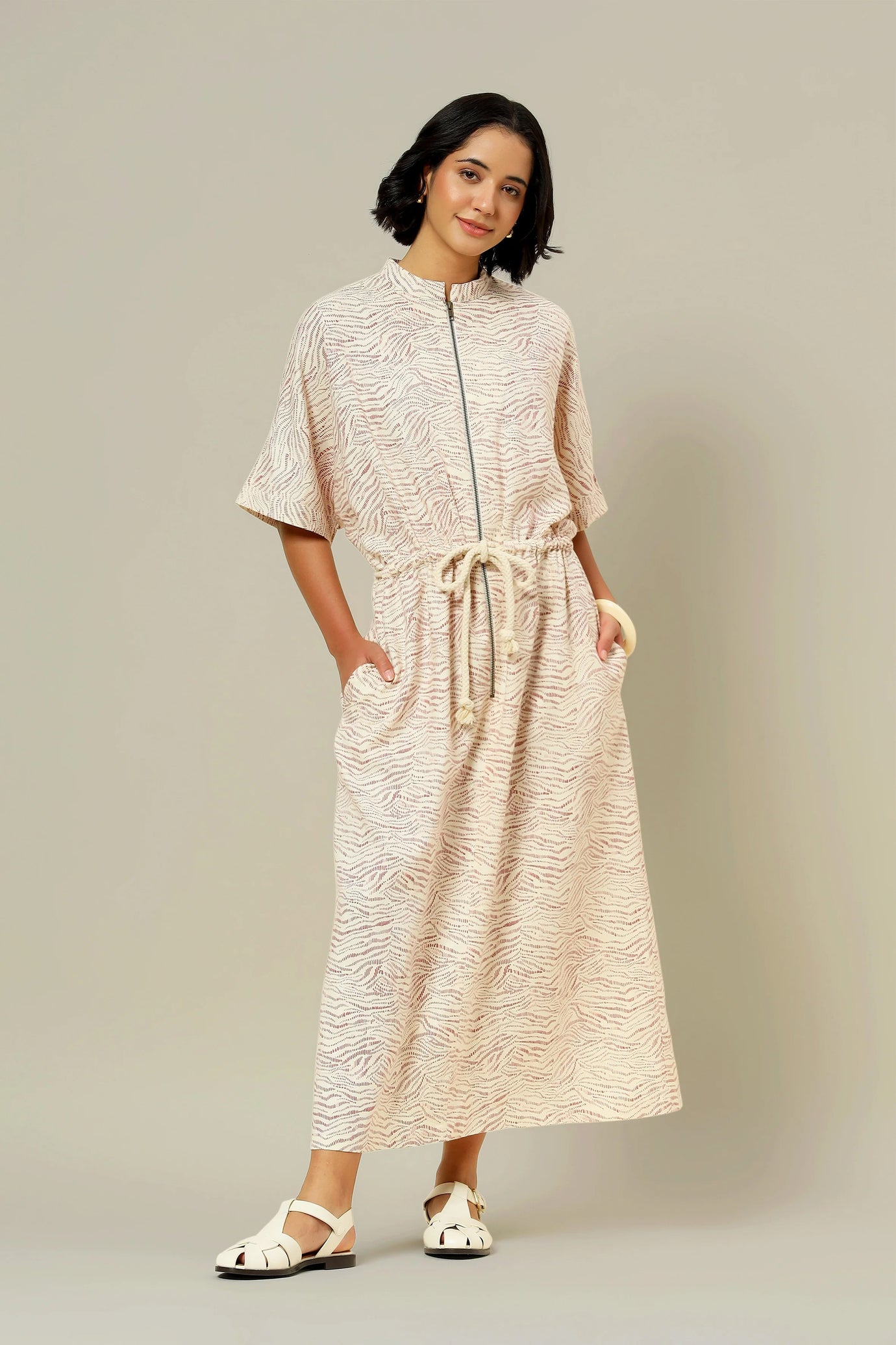 Woman wearing the La Robe Zippée sewing pattern from Atelier Brunette on The Fold Line. A dress pattern made in cotton Oxford, poplin, ikat, woven velvet, linen or linen blends, or cotton gabardine fabric, featuring a stand collar, front zipper, mid length sleeves, cord at the waist, pockets, and ankle length.