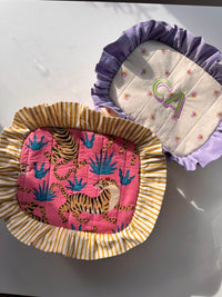 The Layer Cake Bag sewing pattern from Sew Bake Make on The Fold Line. A bag pattern made in linen or cotton fabric, featuring a rectangular shape, ruffles along and edges, and a zipper closure.