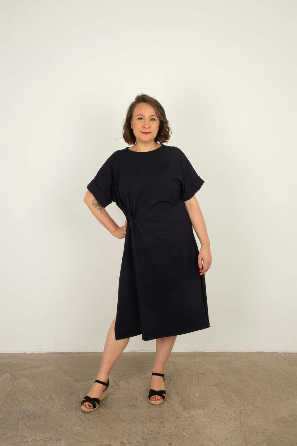 Woman wearing the Layla Dress sewing pattern from Sew Over It on The Fold Line. A dress pattern made in knit fabric, featuring a relaxed fit, round neckline, grown-on short sleeves with cuffs, twist at the waist, side splits, and below knee length.