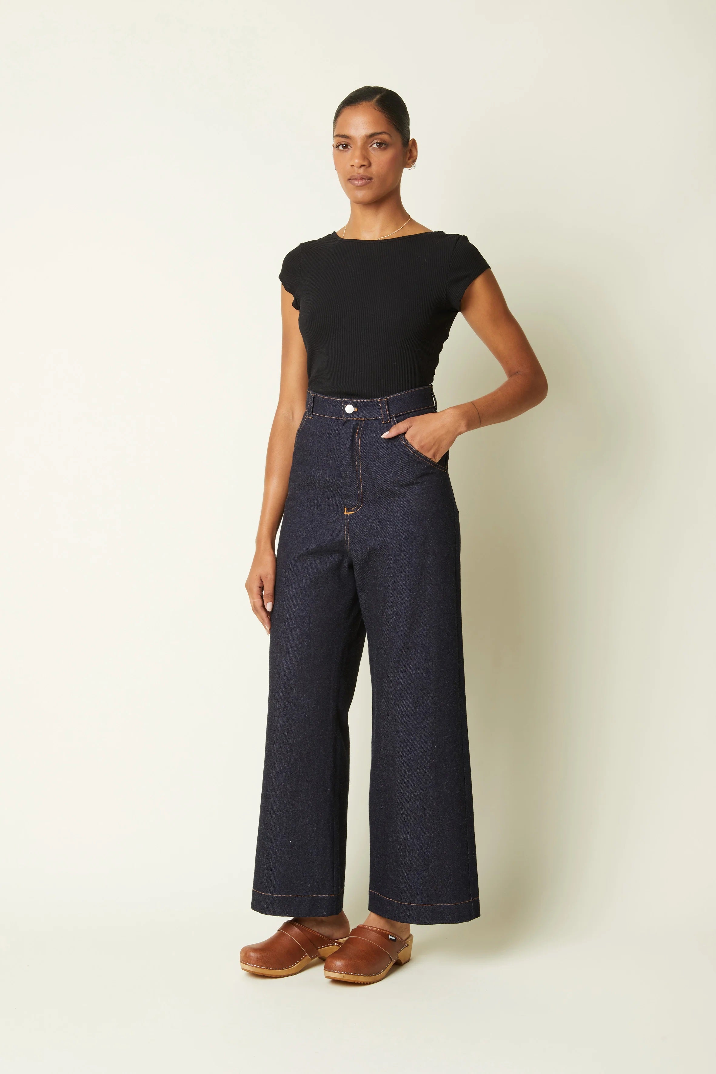 Woman wearing the Le Jean Wide Leg sewing pattern from Atelier Brunette on The Fold Line. A jeans pattern made in denim or thick cotton gabardine fabric, featuring a high waist (above the belly button), wide leg, zipper fly, back yoke, front and back pockets, belt loops, and topstitching.