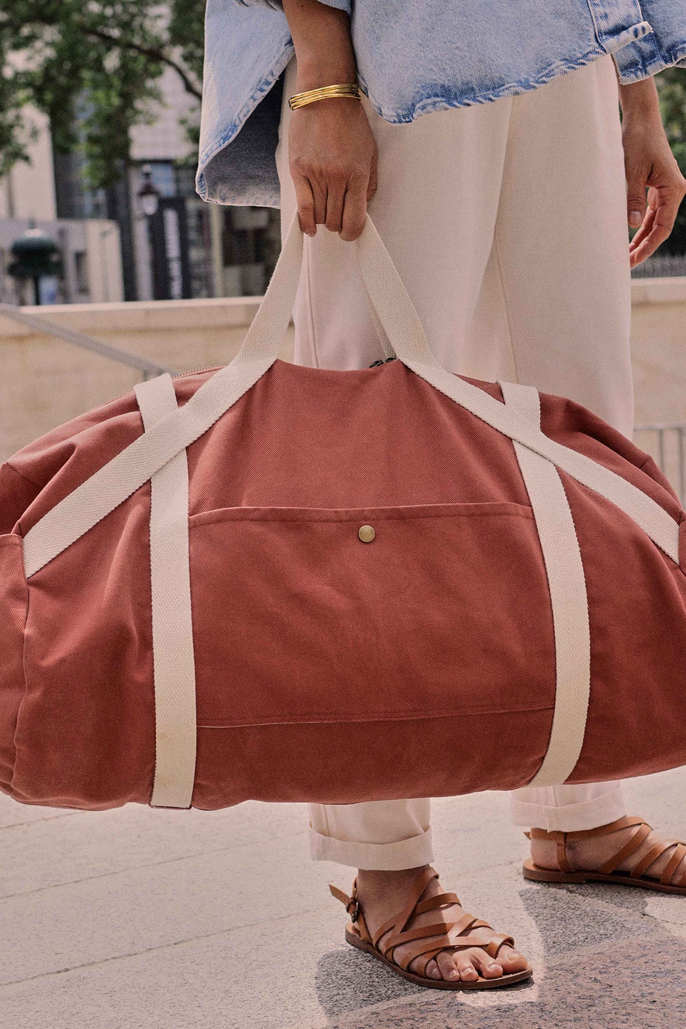 Woman holding the Le Pack Escapade sewing pattern from Atelier Brunette on The Fold Line. A lined bag pattern made in gabardine fabric, featuring a barrel shape, webbing handles, zipper closure, and side pockets with press button closures.