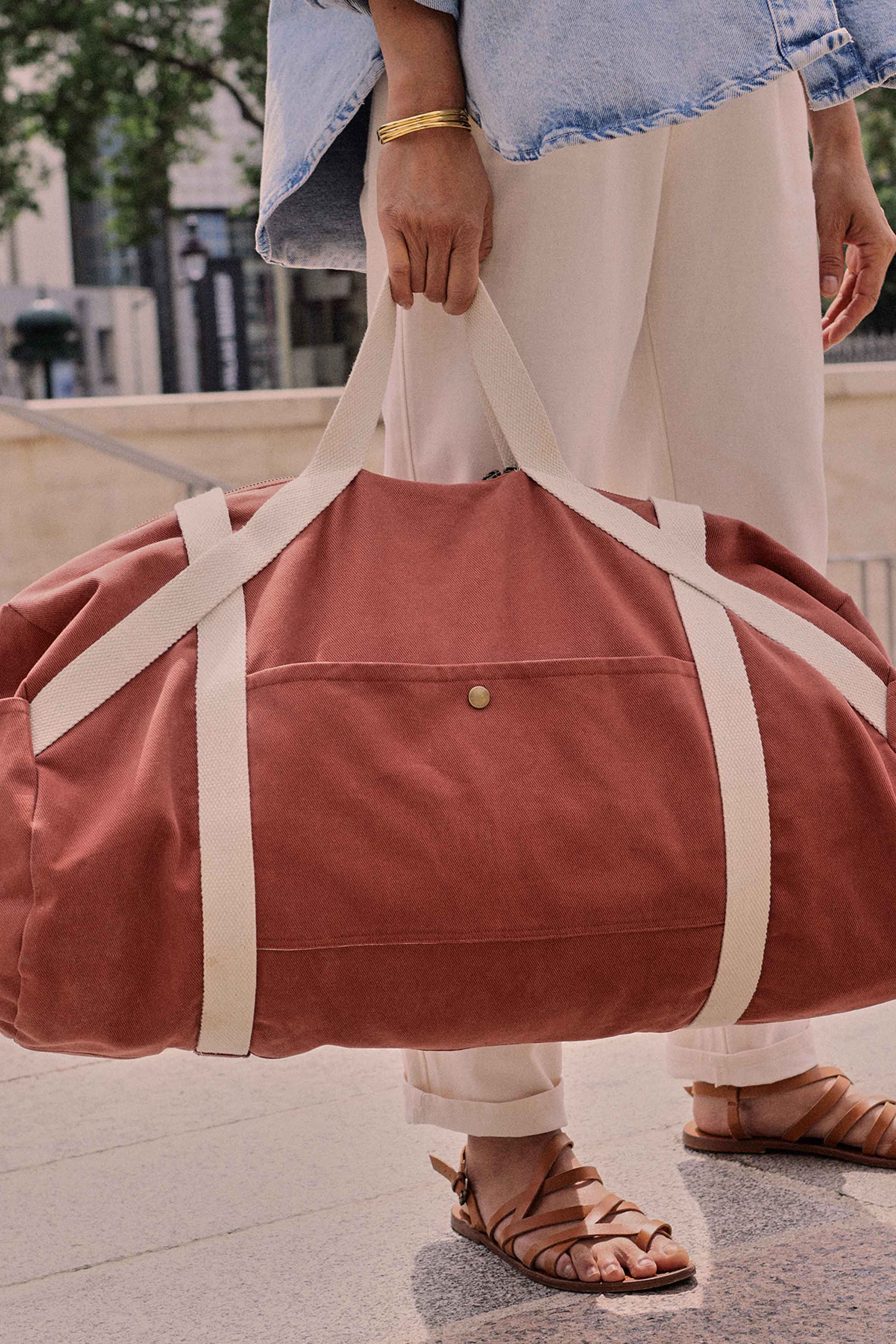 Woman holding the Le Pack Escapade sewing pattern from Atelier Brunette on The Fold Line. A lined bag pattern made in gabardine fabric, featuring a barrel shape, webbing handles, zipper closure, and side pockets with press button closures.