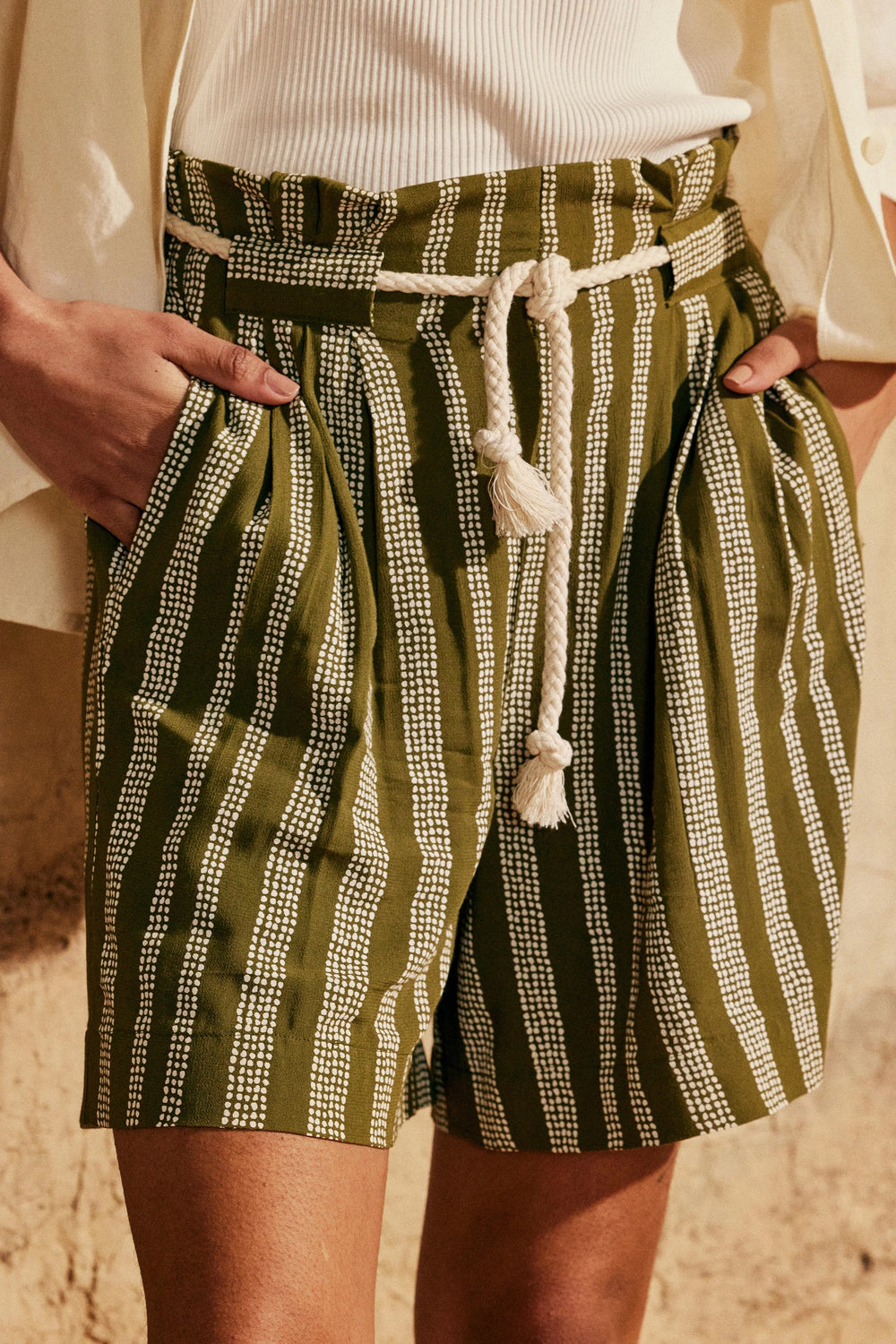 Woman wearing the Le Pantalon Short sewing pattern from Atelier Brunette on The Fold Line. A shorts pattern made in rayon, linen, or cotton/linen blend fabric, featuring a high waist with an elasticated back, front pleats, wide belt loops, and side seam pockets. 