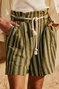 Woman wearing the Le Pantalon Short sewing pattern from Atelier Brunette on The Fold Line. A shorts pattern made in rayon, linen, or cotton/linen blend fabric, featuring a high waist with an elasticated back, front pleats, wide belt loops, and side seam pockets. 