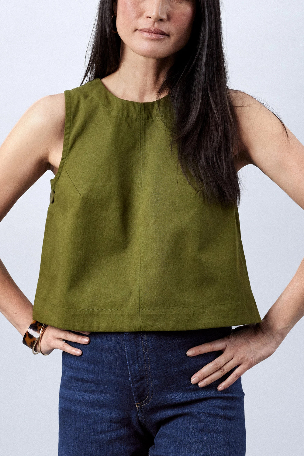 Woman wearing the Le Top sewing pattern from Atelier Brunette on The Fold Line. A sleeveless top pattern made in lightweight gabardine, linen, or cotton fabric, featuring a trapeze shape, round neckline, back invisible zip, and buttons at the sides.