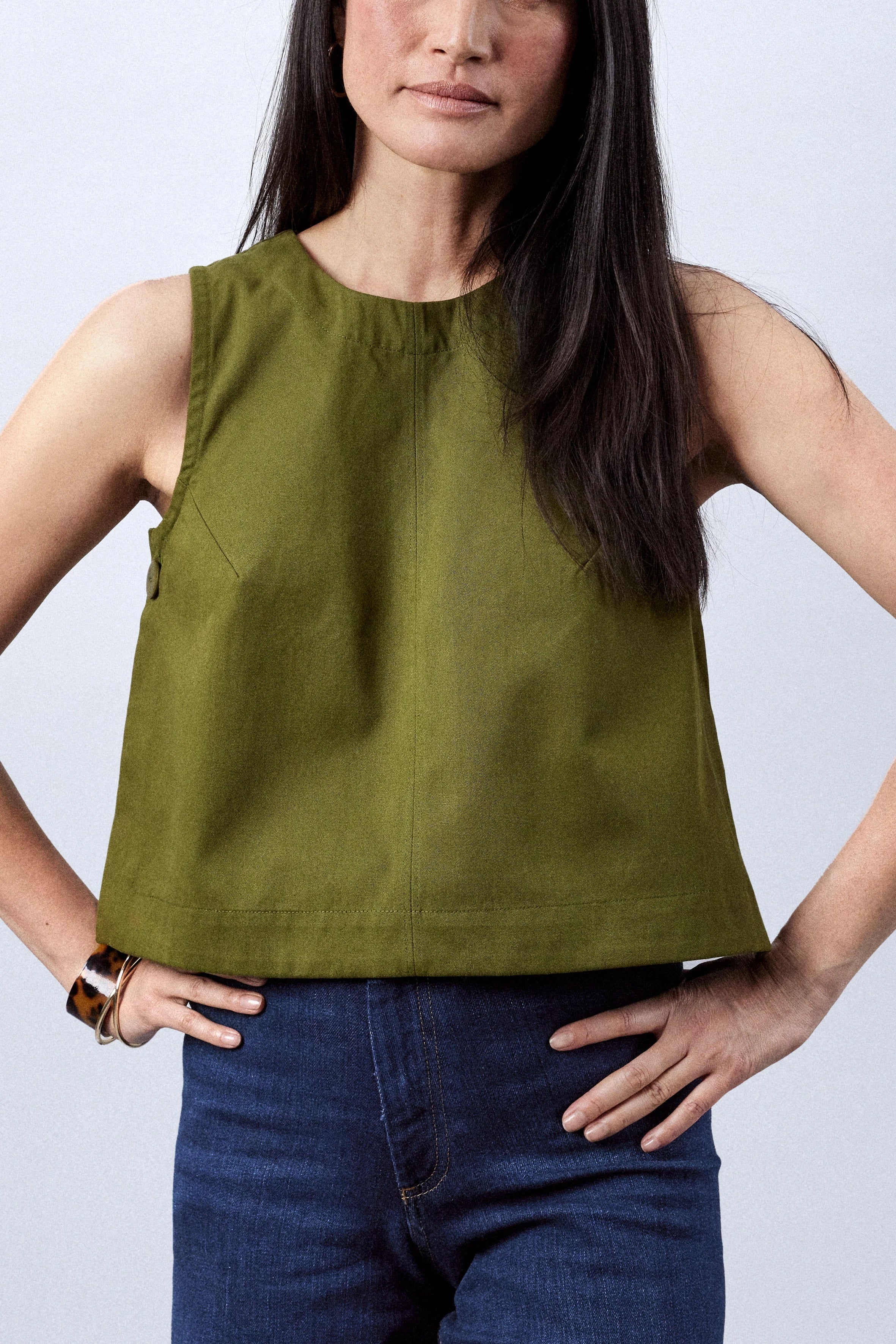 Woman wearing the Le Top sewing pattern from Atelier Brunette on The Fold Line. A sleeveless top pattern made in lightweight gabardine, linen, or cotton fabric, featuring a trapeze shape, round neckline, back invisible zip, and buttons at the sides.