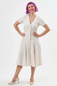 Woman wearing the Lea Dress sewing pattern from Sew Over It on The Fold Line. A tea dress pattern made in rayon, viscose or crepe fabric, featuring a V-neck, fitted bodice, short sleeves with turn ups, panelled skirt, button front closure, and below knee length.